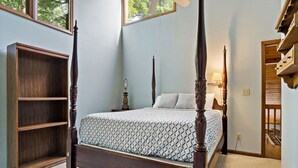 A four-poster bed with a patterned bedspread, a wooden nightstand with a lamp, and a built-in bookshelf. - Pet Friendly, Private Wooded Setting - Travelers Rest by Carolina Properties (Rutherfordton)