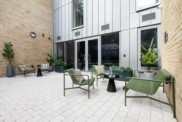 An outdoor seating area with green metal chairs and tables, surrounded by potted plants and a brick wall. - Student Only Huxley Studios (Edinburgh)