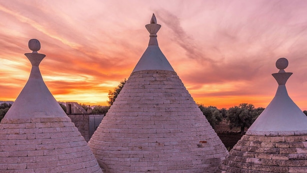 A rooftop with three conical tents, a small table with a lamp, and a bench with cushions.