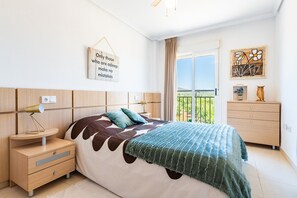 A bedroom with a bed, bedside table, lamp, dresser, and a balcony view.