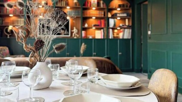 Un comedor con una mesa redonda dispuesta para cuatro personas, rodeada de sillas. Un jarrón con flores secas se coloca sobre la mesa.