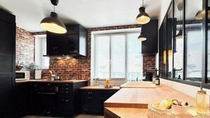 Una cocina moderna con gabinetes negros, pared de ladrillo e iluminación colgante.