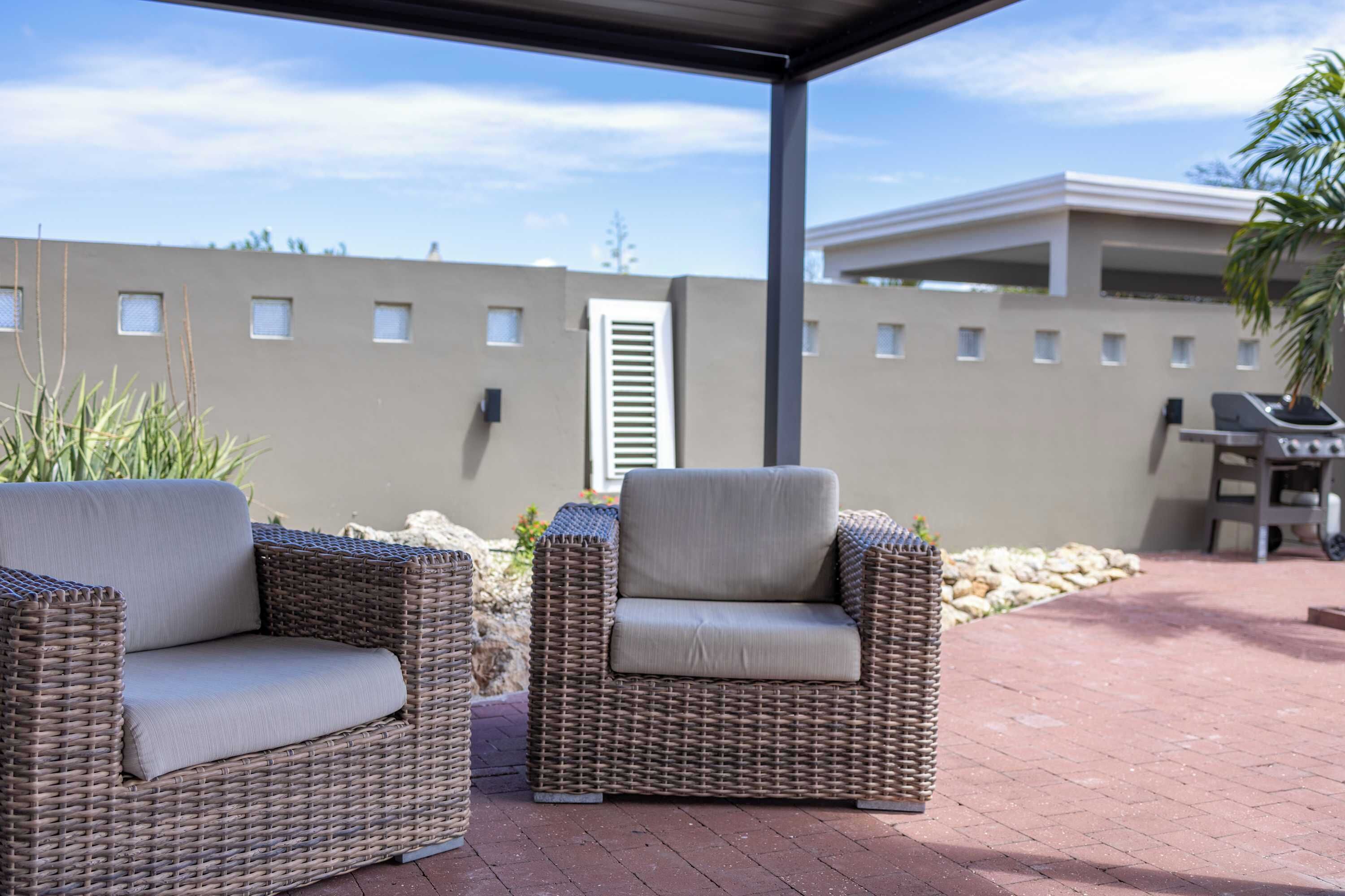 Een overdekt terras met rieten meubels en een stenen muur op de achtergrond.