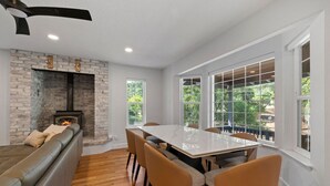 Una cocina moderna con chimenea de piedra, una mesa de comedor con sillas y ventanas amplias con vistas al exterior.