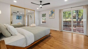 Un dormitorio amplio con una cama grande, un ventilador de techo y un ventanal corredero que da a un espacio exterior.
