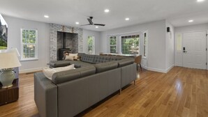 Un amplio salón con un sofá modular grande, una chimenea y grandes ventanales con vistas al exterior.