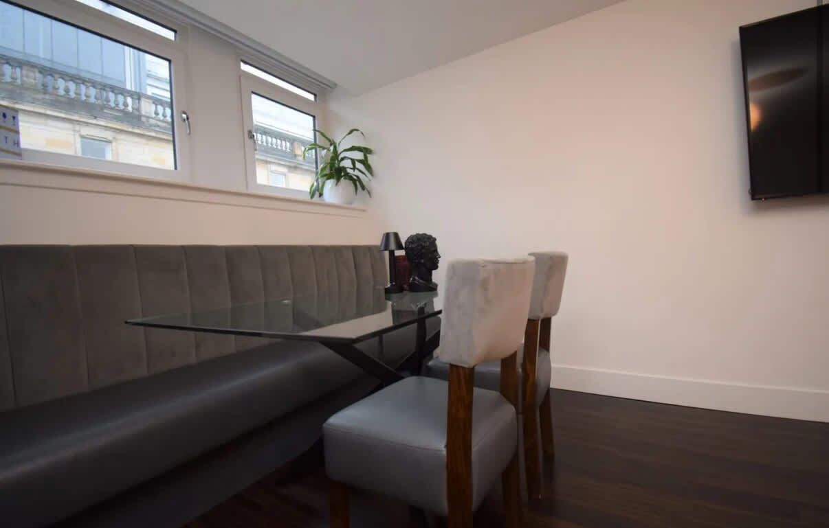 A modern living room with a grey sofa, a glass coffee table, and a TV mounted on the wall.