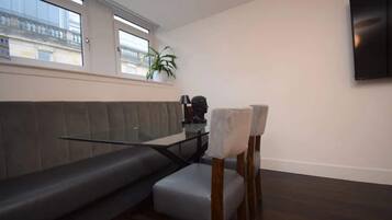 A modern living room with a grey sofa, a glass coffee table, and a TV mounted on the wall.