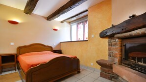 A bedroom with a wooden bed, a fireplace, and a window with curtains. - Holiday Home 'La Charrue' with Mountain View, Shared Pool and Wi-Fi (Villecomtal)