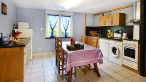 A kitchen with a dining table, chairs, a washing machine, and a stove. - Holiday Home 'La Charrue' with Mountain View, Shared Pool and Wi-Fi (Villecomtal)