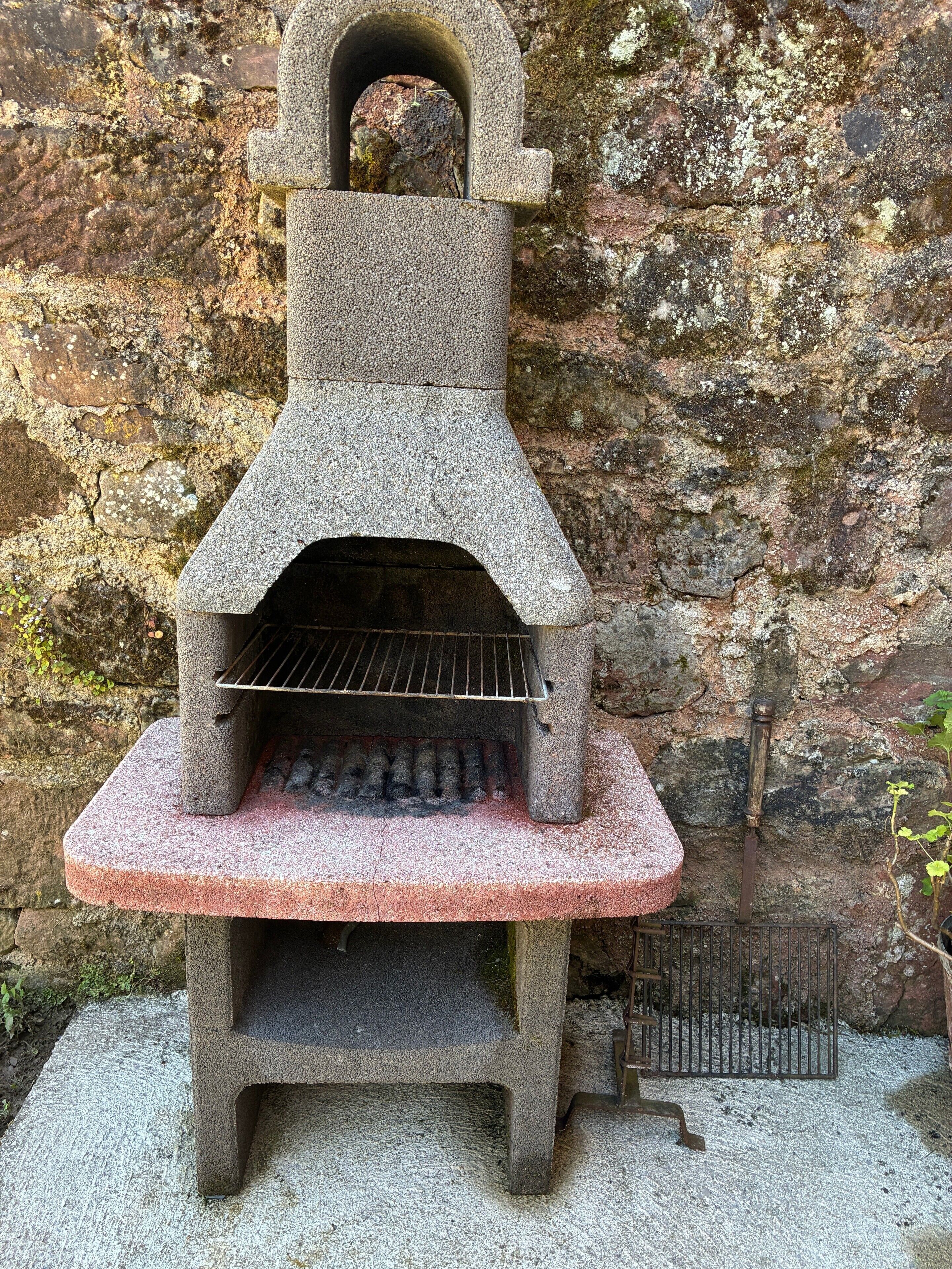 Un barbecue extérieur en pierre, doté d’une cheminée, installé contre un mur rocheux.