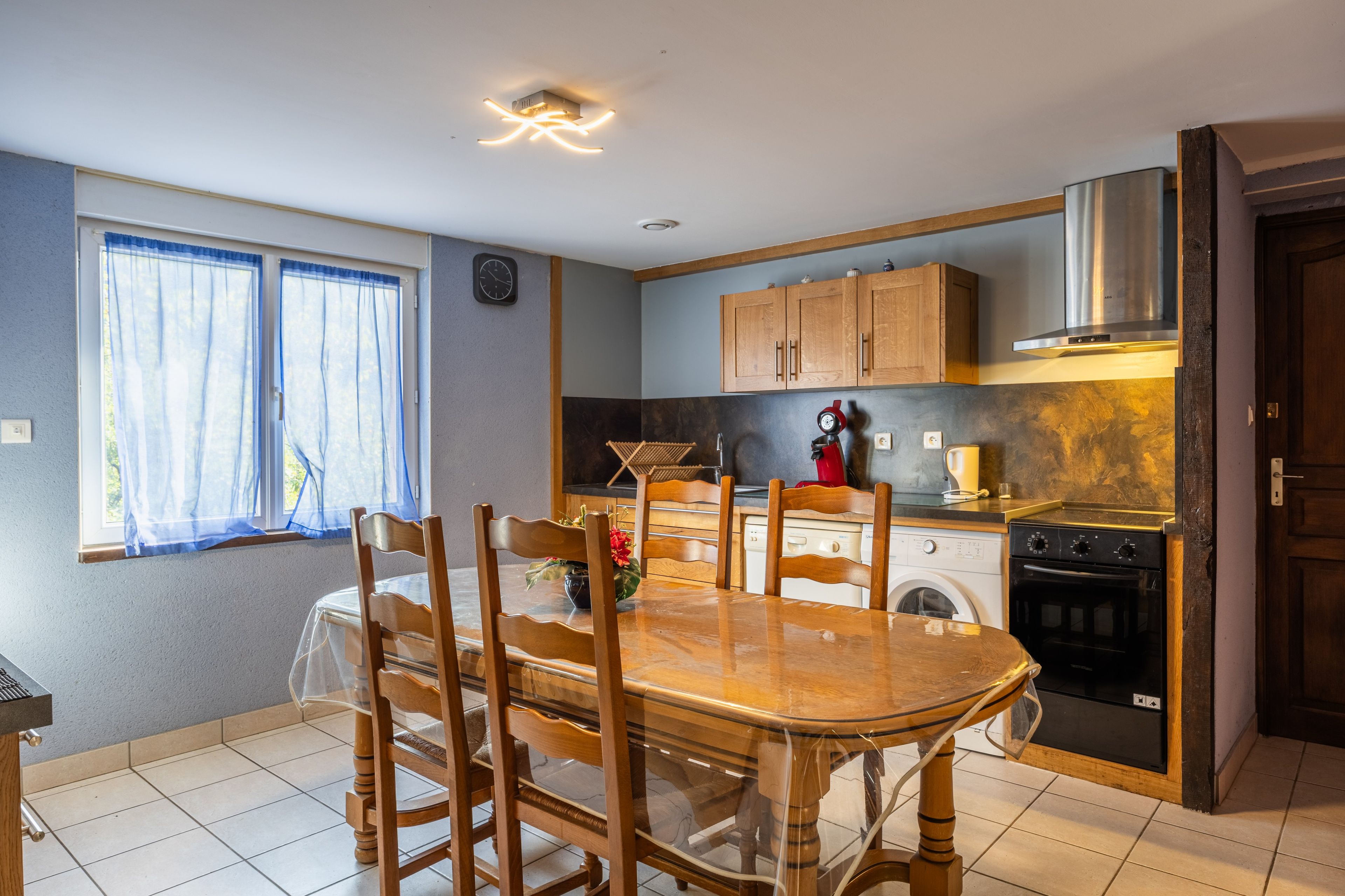 Une cuisine compacte comprenant une table à manger, des chaises, un lave-linge, une cuisinière et une horloge murale.