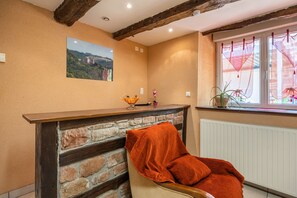 A room with a fireplace, a chair with an orange blanket, a window with lace curtains, and a painting on the wall. - Holiday Home 'La Charrue' with Mountain View, Shared Pool and Wi-Fi (Villecomtal)