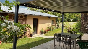 A covered patio area with a table and chairs, a stone building, and potted plants. - Holiday Home 'La Charrue' with Mountain View, Shared Pool and Wi-Fi (Villecomtal)