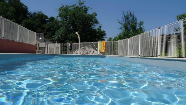 A swimming pool with clear water, surrounded by a metal fence and trees in the background. - Holiday Home 'La Charrue' with Mountain View, Shared Pool and Wi-Fi (Villecomtal)