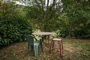 An outdoor seating area with a round table and two chairs, surrounded by dense foliage.