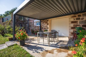 A covered patio area with a table and chairs, surrounded by potted plants and a stone wall. - Holiday Home 'La Charrue' with Mountain View, Shared Pool and Wi-Fi (Villecomtal)