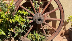 A large wooden wheel with spokes, surrounded by greenery and a stone wall. - Holiday Home 'La Charrue' with Mountain View, Shared Pool and Wi-Fi (Villecomtal)