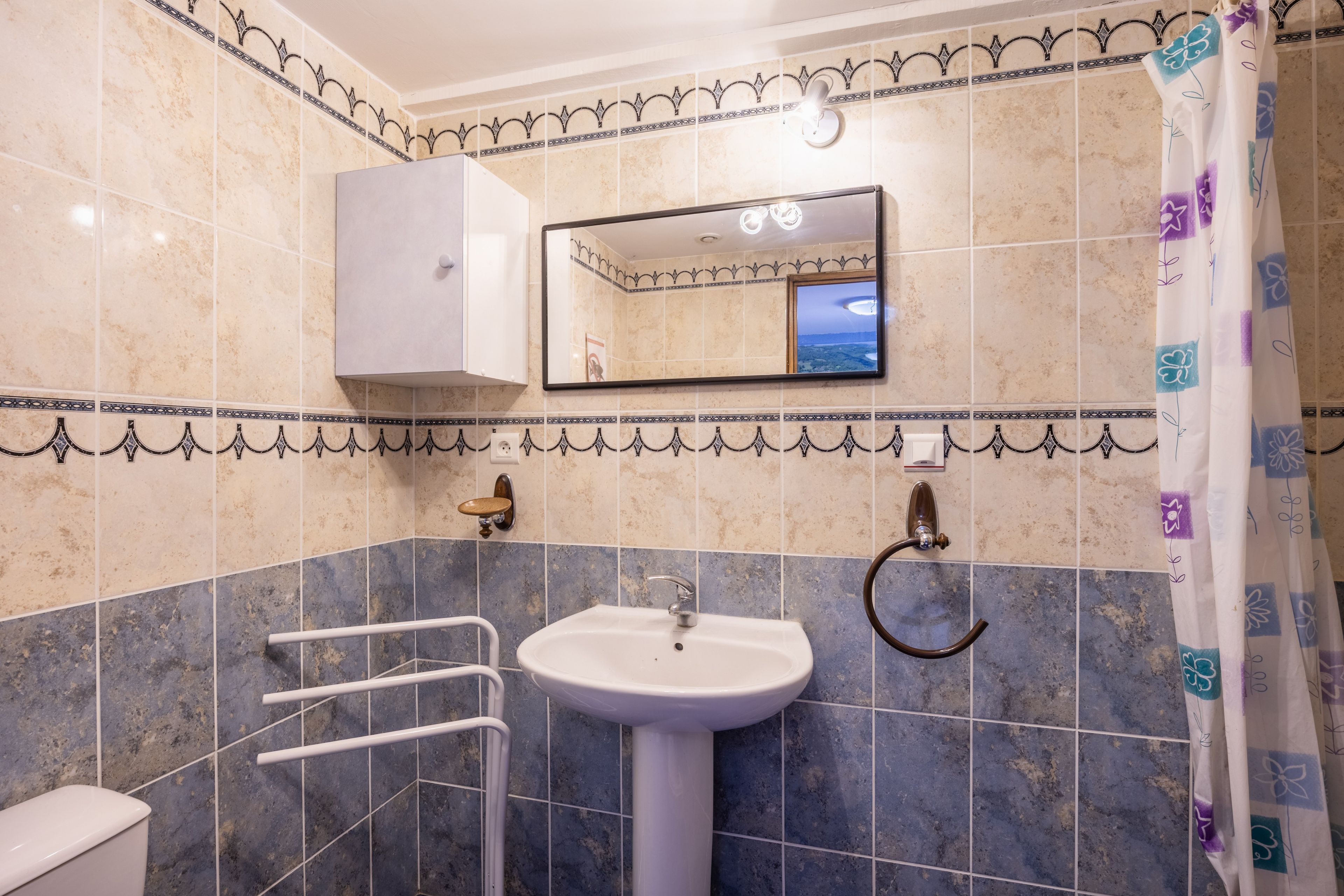 Un baño con lavamanos blanco, espejo, toallero y cortina de ducha.