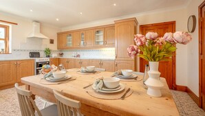 A kitchen with wooden cabinets, a dining table set for four, and a vase of flowers on the table.