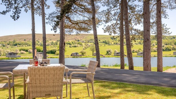 A table set outdoors with chairs, overlooking a lake and hills.