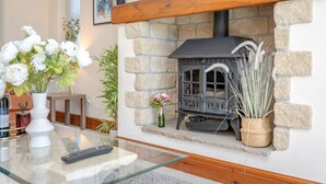 A stone fireplace with a black stove, surrounded by a white wall and a wooden mantel.
