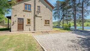 A stone building with a wooden door and windows, a gravel driveway, and a view of a lake and trees.
