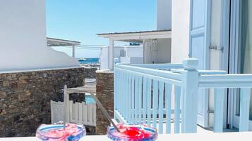 A balcony with two drinks on a blue table, overlooking a pool and buildings with white and blue architecture.