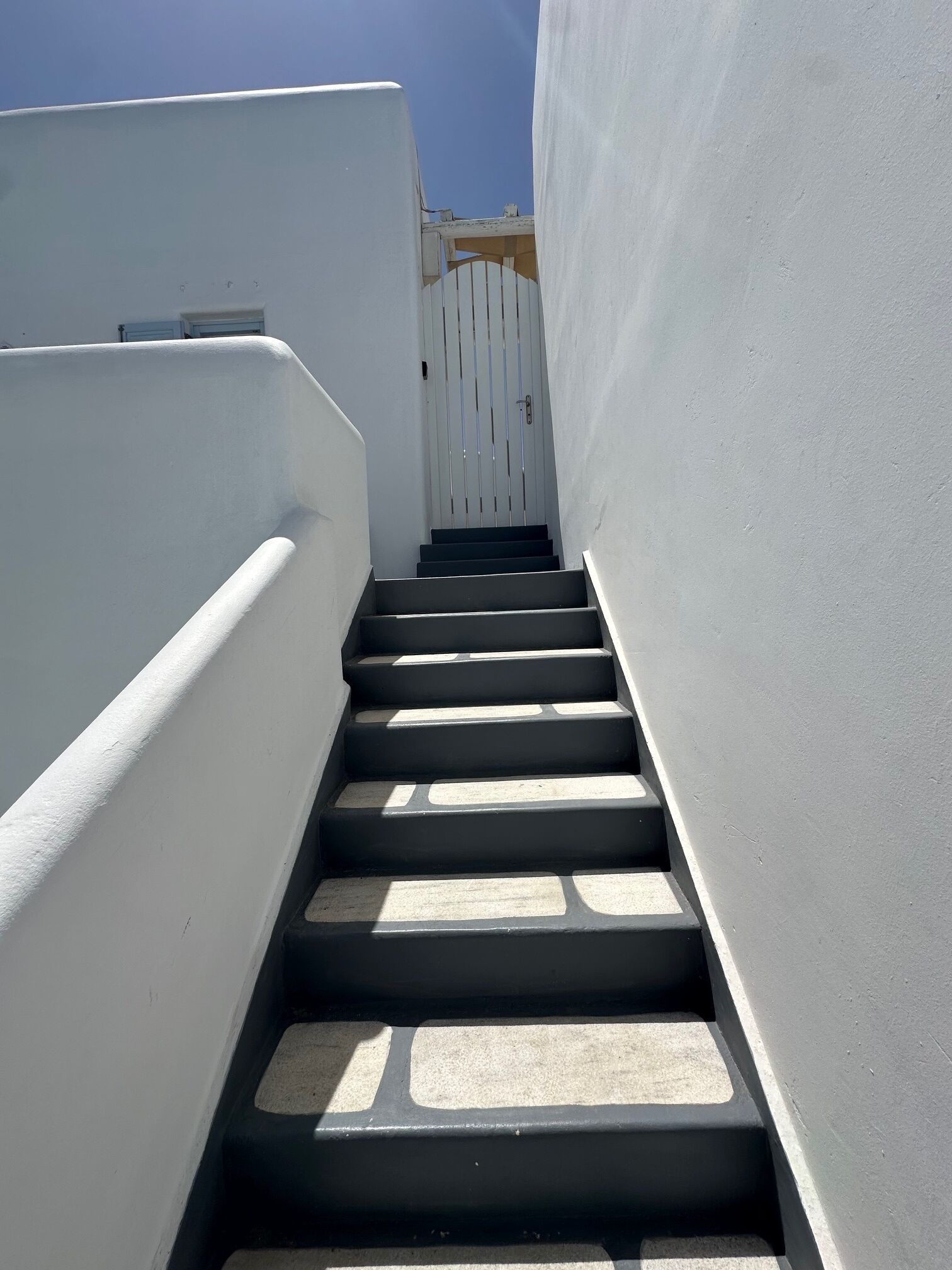 Una escalera estrecha, pintada de blanco, que lleva a una puerta con un portón blanco.