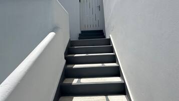 Una escalera estrecha, pintada de blanco, que lleva a una puerta con un portón blanco.