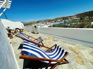 Una terraza en la azotea con sillones a rayas, suelo de piedra y vistas a un pueblo costero.