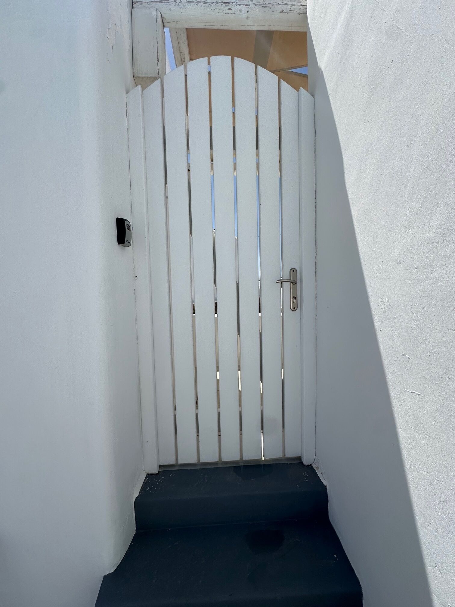 A white gate with vertical slats and a metal handle, leading to a dark staircase.