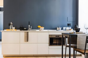 A modern kitchen with a dark blue wall, a white countertop, and a dining area with a table and chairs. - Apartment 'De Gasperi' with Balcony, Wi-Fi and Air Conditioning (Bari)