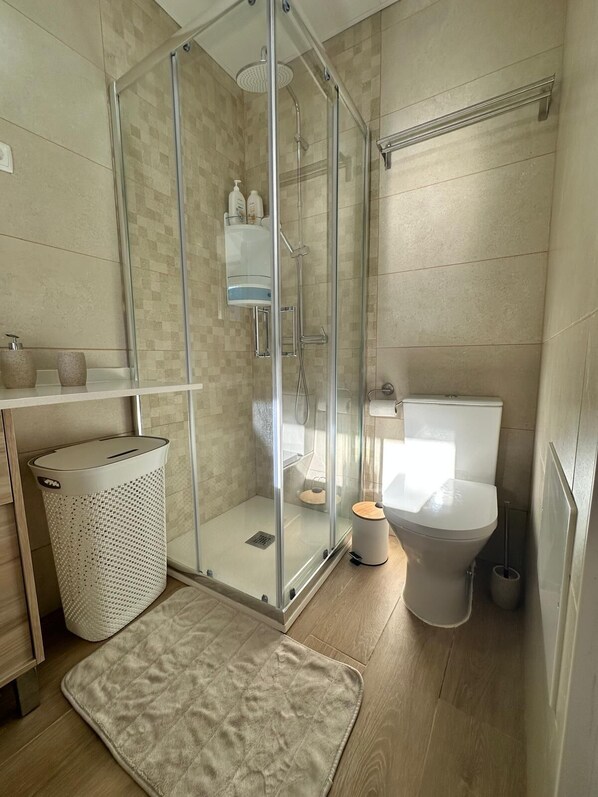 Une salle de bain moderne avec une douche à parois de verre, des toilettes, un lavabo et une poubelle.