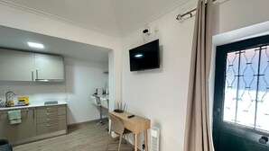 Een kleine hotelkamer met kitchenette, een bed, bureau met stoel, televisie en raam met gordijnen.