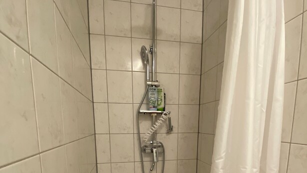 Zona de ducha con cabezal de ducha manual, grifo empotrado y un estante con artículos de aseo.