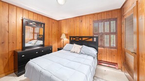 Een slaapkamer met houten wanden, een bed met witte dekbedovertrek, een nachtkastje, een spiegel en een raam met luiken.