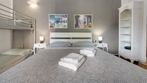 A hotel room with a bunk bed, a large bed with a patterned bedspread, two bedside tables with lamps, and a white wardrobe. - Apartment 'La Terrazza Di Basilio' with Lake View, Balcony and Wi-Fi (Olginate)