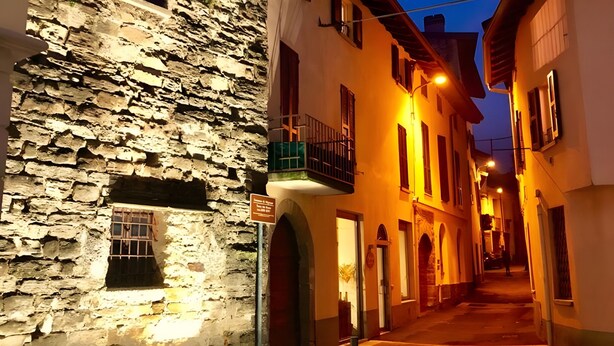 A narrow street with stone buildings, a signpost, and a paved path. - Apartment 'La Terrazza Di Basilio' with Lake View, Balcony and Wi-Fi (Olginate)