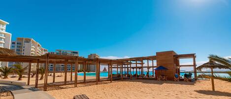 Une plage avec des structures en bois, une piscine et une vue sur l’océan.