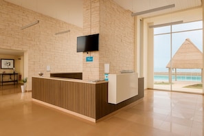 Una recepción con un televisor de pantalla plana en la pared, un letrero que indica un área de spa y vistas a la playa a través de grandes ventanales.