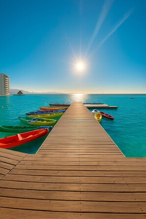 A wooden pier leading to a calm sea with several colorful kayaks lined up.