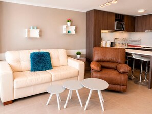 A modern living room with a sofa, a brown leather chair, and two small tables.
