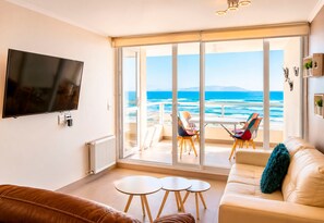 A living room with a large TV, a sofa, two small tables, and a balcony with a view of the sea. - Smart Host Rentals - A paradise for your family! (La Serena)