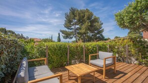 A wooden deck with two chairs and a table, surrounded by greenery and trees.