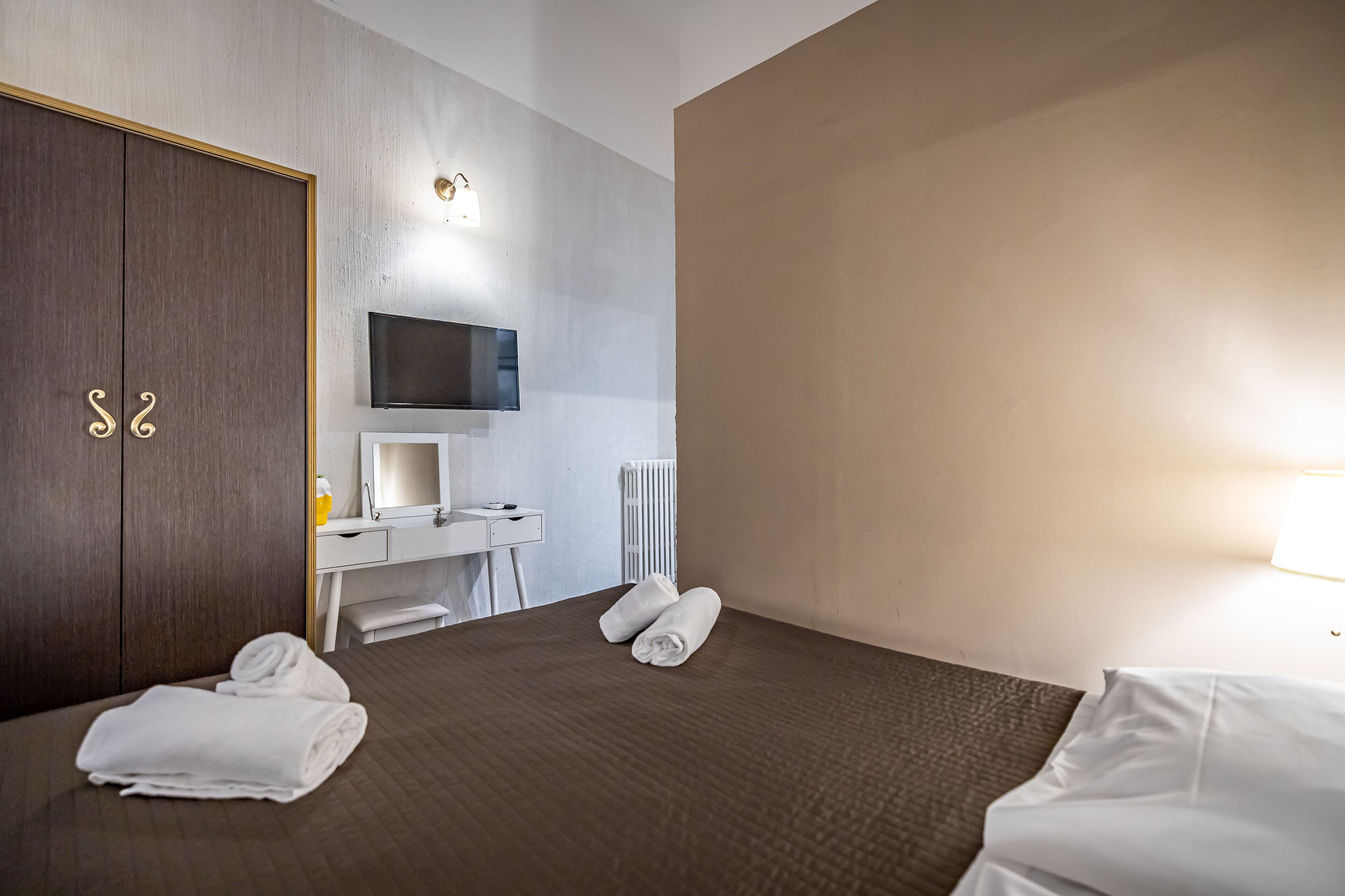 Ein Hotelzimmer mit einem Bett, einem Schreibtisch mit Computer, einem Fernseher und einem Kleiderschrank.