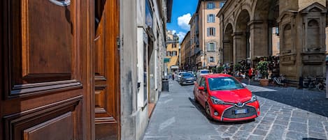 Una calle estrecha con edificios históricos, un coche rojo estacionado al lado y pavimento adoquinado.