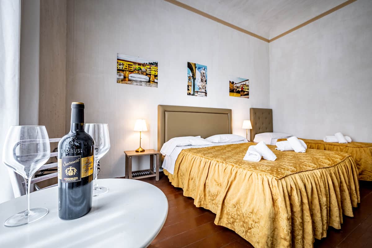 A hotel room with two beds, a table with a bottle of wine, and two lamps.