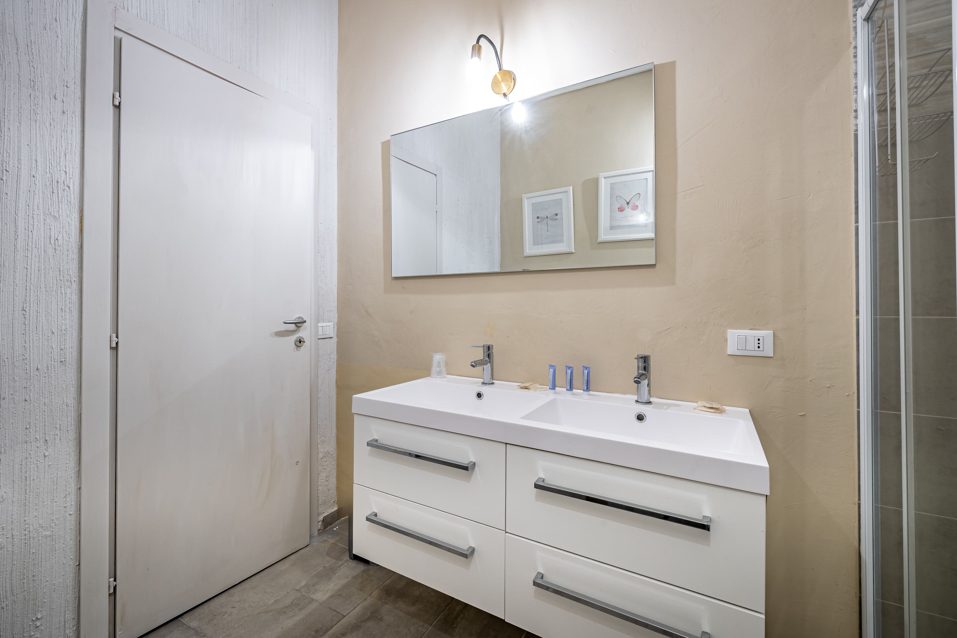 Un bagno con un mobile lavabo bianco, due lavandini, uno specchio grande e uno spazio doccia.