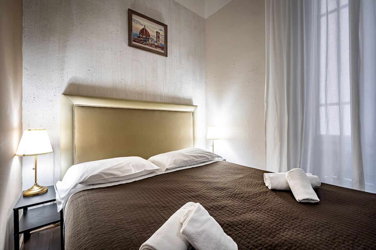 A neatly made bed with a brown quilt, white pillows, and rolled towels on a headboard.